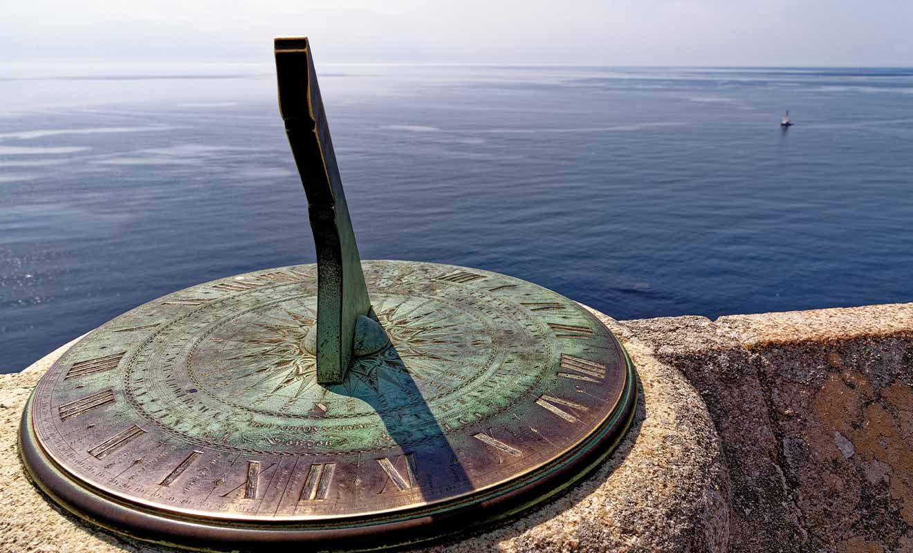 sundial sitting on a wall in front of a large body of water