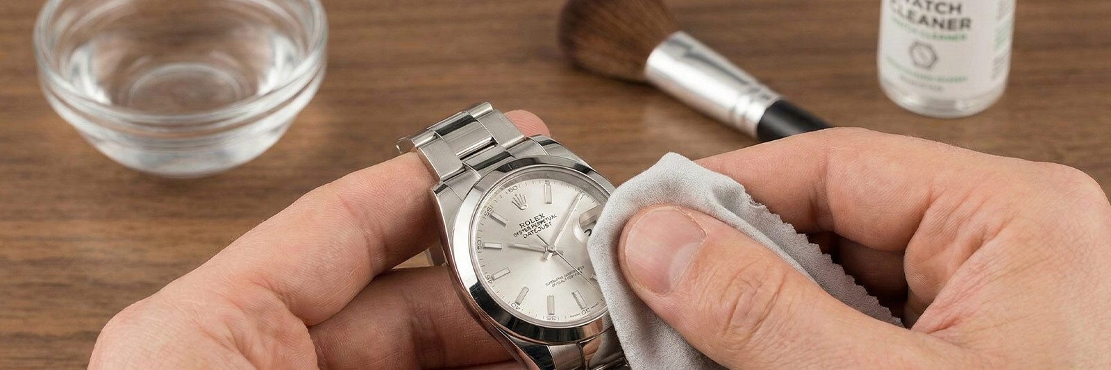 Close-up view of hands safely cleaning a stainless steel Rolex Datejust using a soft microfiber cloth to remove daily buildup and fingerprints.