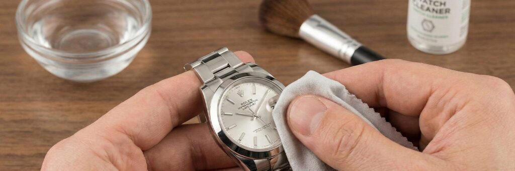 Close-up view of hands safely cleaning a stainless steel Rolex Datejust using a soft microfiber cloth to remove daily buildup and fingerprints.